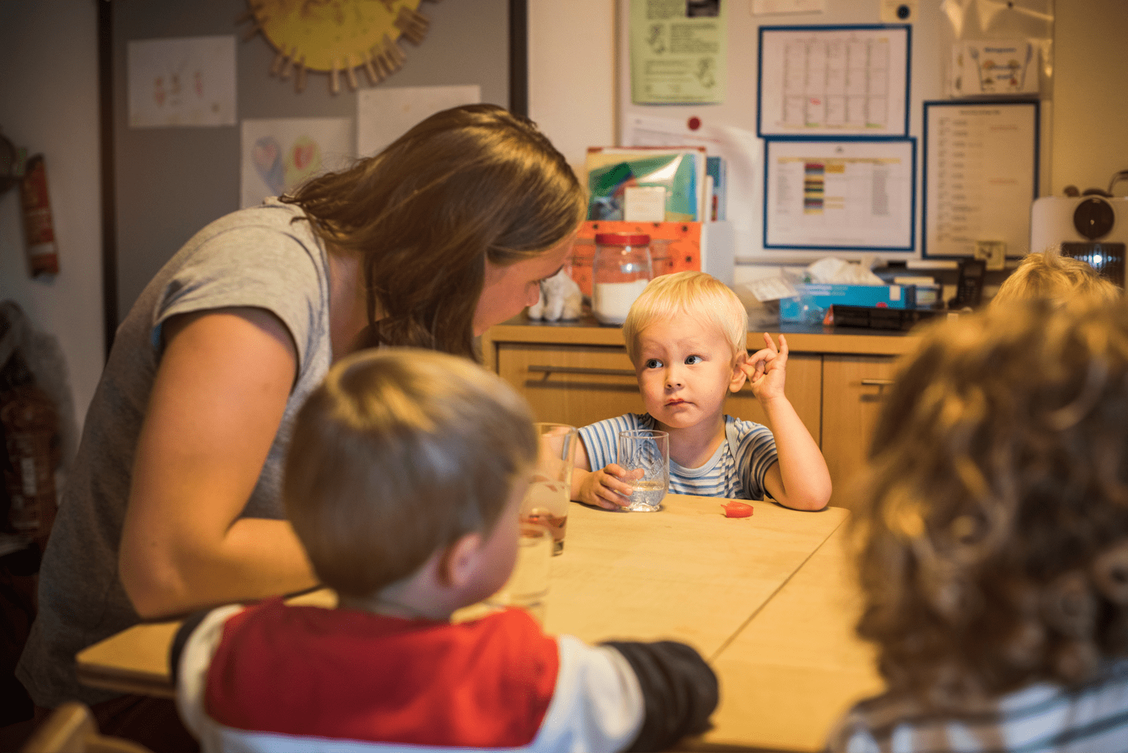 Kita-Betreuerin plaudert mit Kindern am Tisch