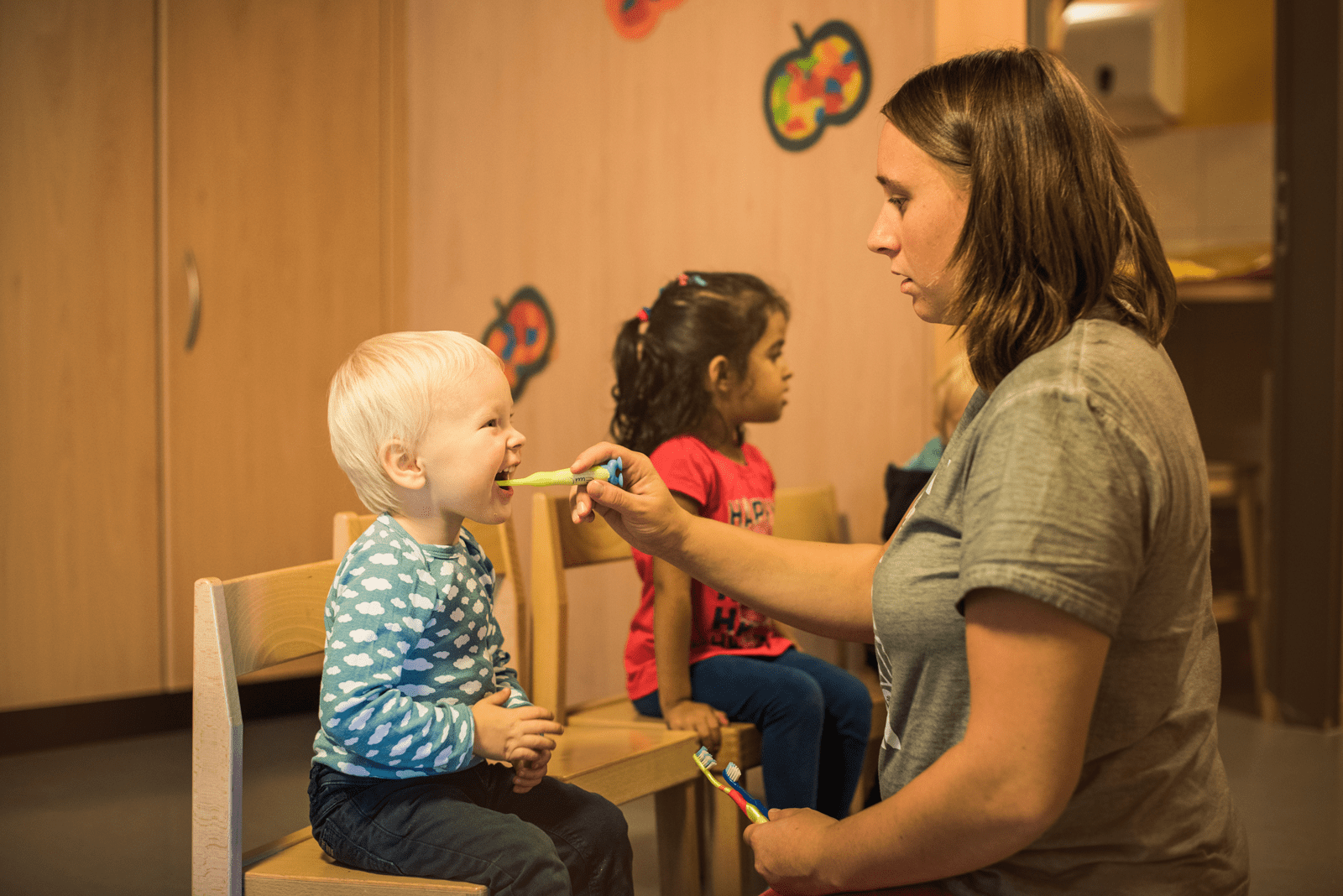 Kinderbetreuerin putzt Knabe die Zähne und singt dazu ein Zahnputzlied.