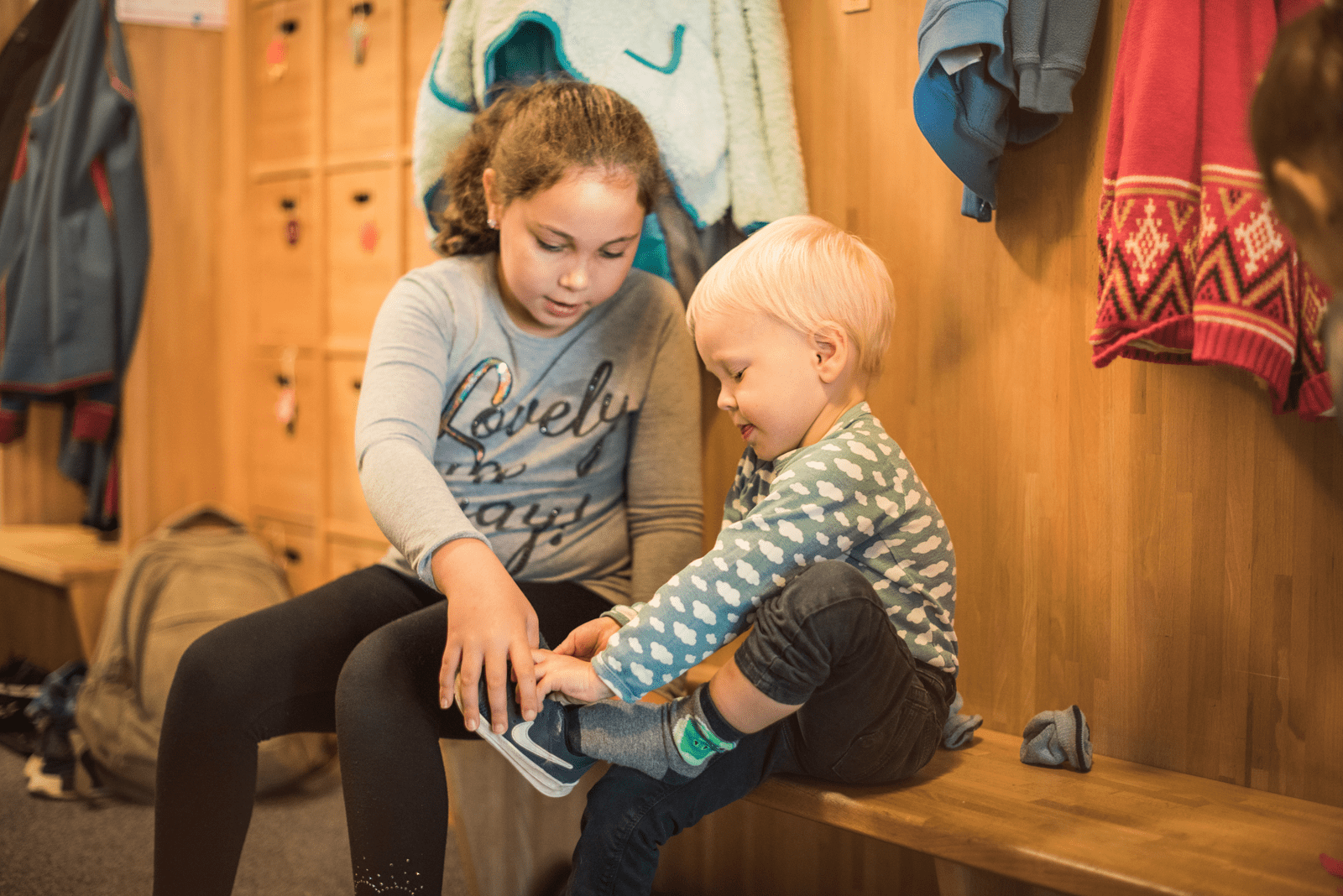 Mädchen aus Kindertagesstätte hilft einem Jungen die Schuhe anzuziehen.